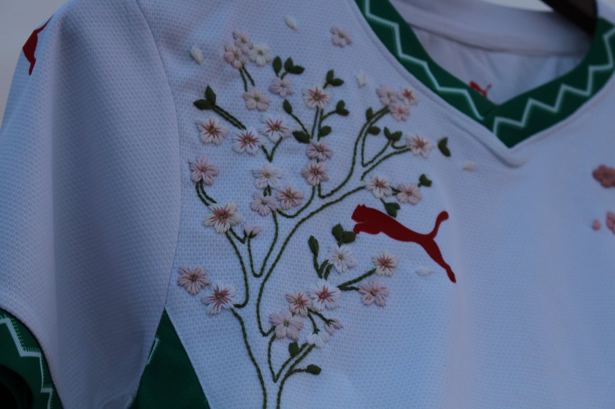 Embroidered design on white fabric showing delicate flowering branch with red bird in flight